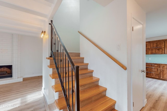 stairway featuring beam ceiling, wood finished floors, baseboards, and a large fireplace