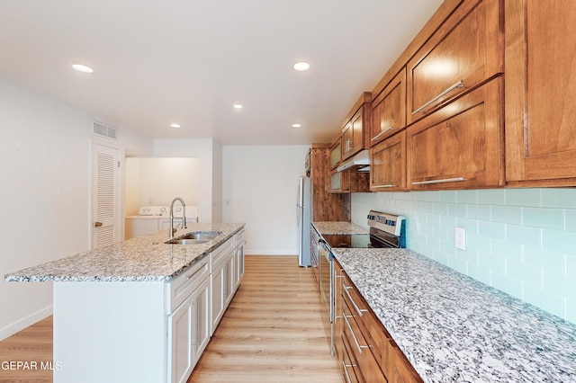 kitchen featuring a kitchen island with sink, a sink, stainless steel range with electric stovetop, light wood-style floors, and under cabinet range hood