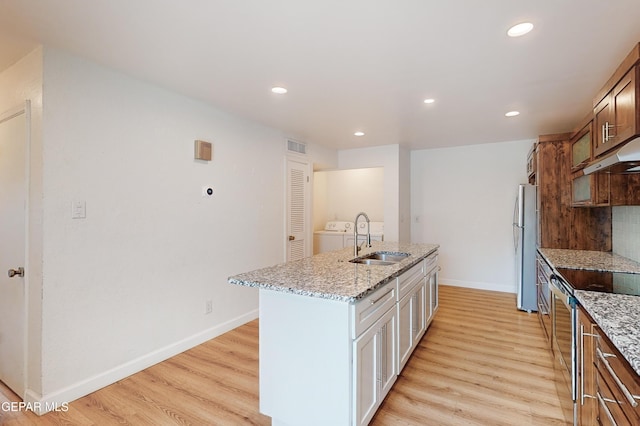 kitchen with a sink, stainless steel appliances, light wood-style floors, and an island with sink