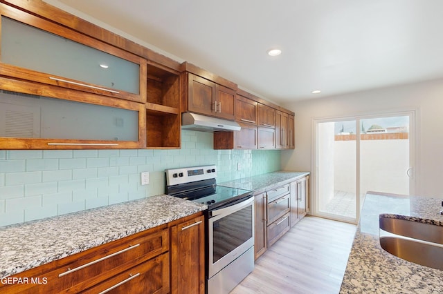 kitchen with light stone countertops, a sink, electric stove, under cabinet range hood, and light wood-type flooring