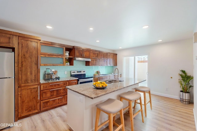 kitchen with a breakfast bar area, a sink, under cabinet range hood, appliances with stainless steel finishes, and backsplash