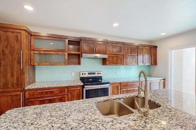 kitchen featuring stainless steel electric range oven, light stone countertops, a sink, under cabinet range hood, and tasteful backsplash