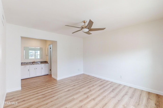 spare room featuring a sink, baseboards, light wood-style flooring, and a ceiling fan