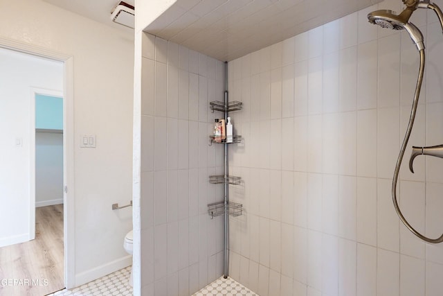 bathroom featuring a tile shower, toilet, and baseboards