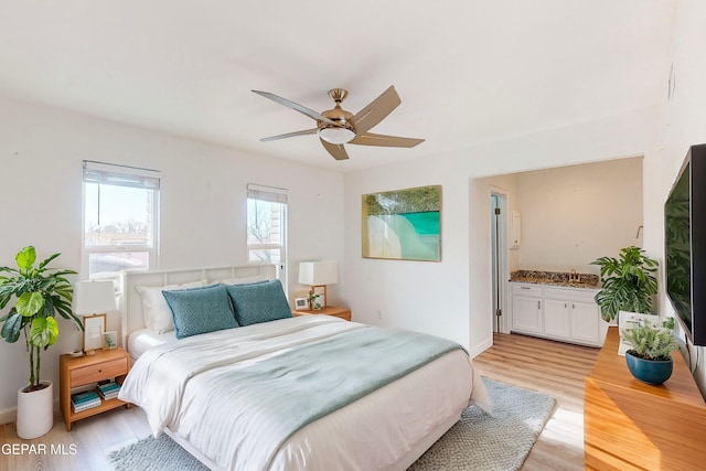 bedroom featuring baseboards, ceiling fan, a sink, light wood-style floors, and connected bathroom