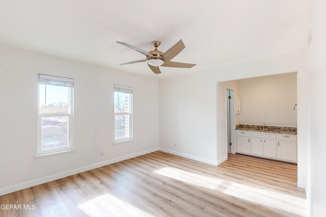 spare room featuring light wood-style flooring, a ceiling fan, baseboards, and a sink