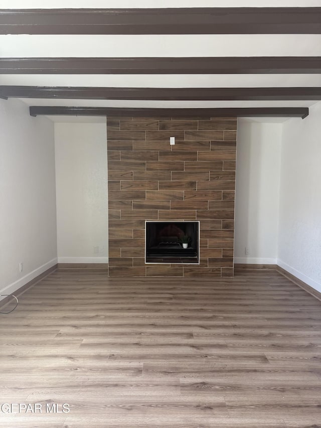 unfurnished living room featuring beam ceiling, light wood finished floors, baseboards, and a tile fireplace