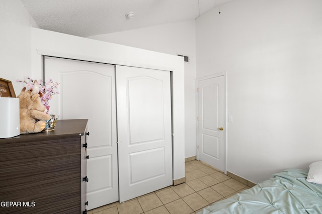 bedroom with a closet, visible vents, light tile patterned flooring, vaulted ceiling, and a textured ceiling