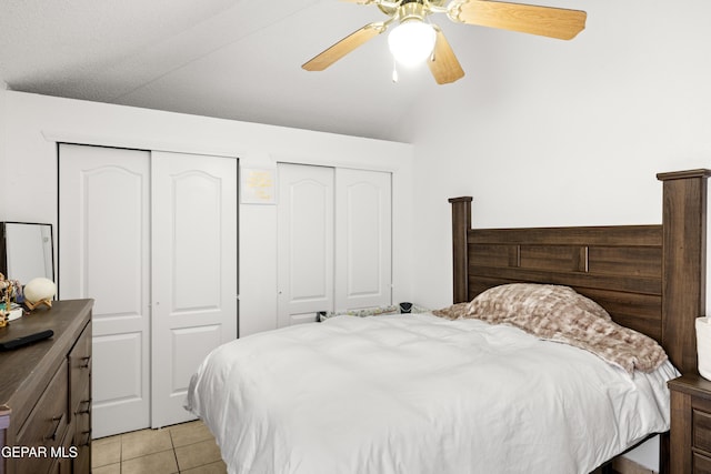 bedroom with ceiling fan, vaulted ceiling, multiple closets, and light tile patterned flooring