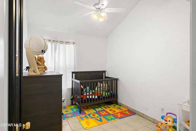 bedroom featuring ceiling fan, lofted ceiling, baseboards, tile patterned floors, and a crib