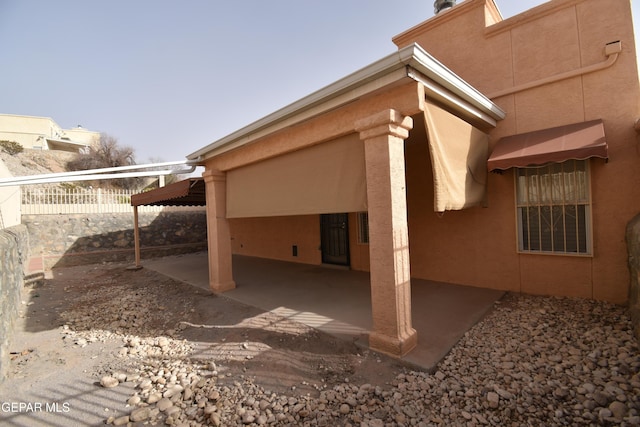 view of property exterior with stucco siding, fence, and a patio