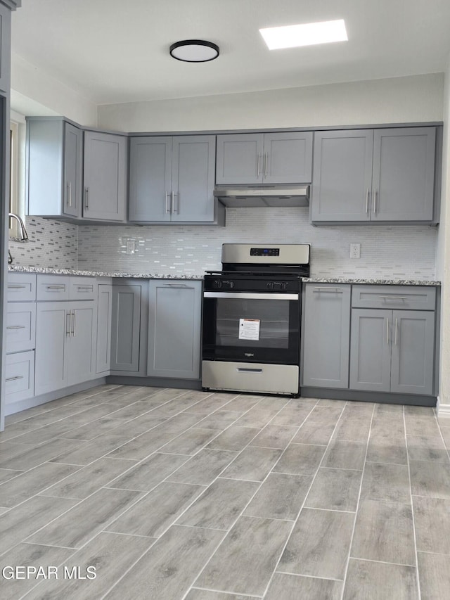 kitchen with under cabinet range hood, stainless steel range with gas cooktop, decorative backsplash, and gray cabinetry