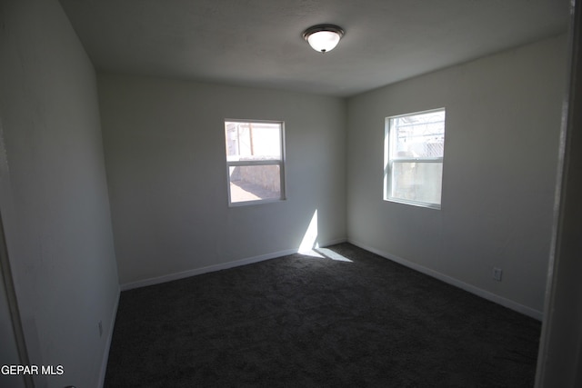 spare room with plenty of natural light, dark carpet, and baseboards