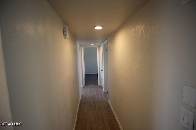 hallway with a textured wall, wood finished floors, visible vents, and baseboards