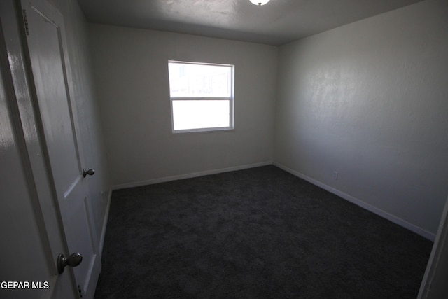 spare room featuring dark carpet and baseboards