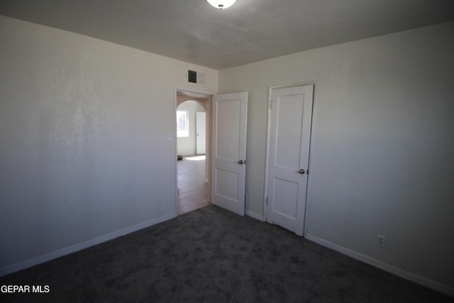 unfurnished bedroom with arched walkways, baseboards, visible vents, and carpet