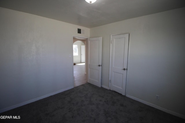 carpeted empty room featuring baseboards, visible vents, and arched walkways