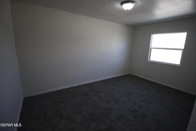 empty room featuring baseboards and dark colored carpet