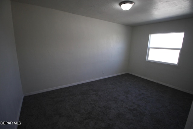 empty room featuring dark colored carpet and baseboards