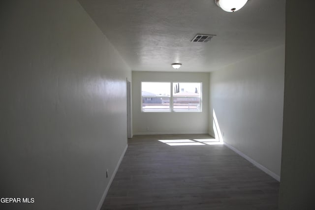 empty room with visible vents, a textured ceiling, baseboards, and wood finished floors