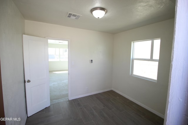 empty room with baseboards, dark wood-style flooring, visible vents, and a healthy amount of sunlight