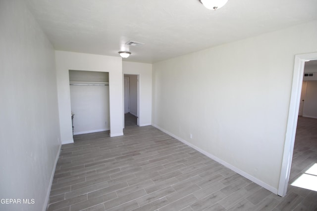 unfurnished bedroom with a closet, wood finished floors, visible vents, and baseboards