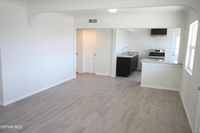 interior space with arched walkways, visible vents, a sink, light wood-type flooring, and baseboards