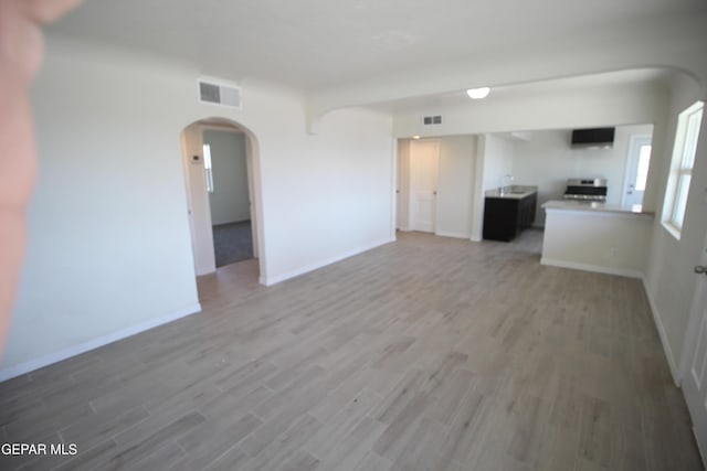 unfurnished living room featuring arched walkways, visible vents, and light wood-style flooring