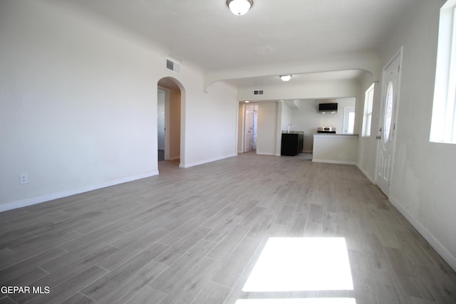 unfurnished living room with light wood-type flooring, arched walkways, visible vents, and baseboards