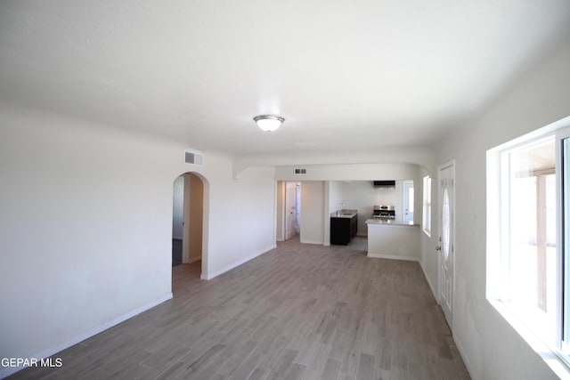 unfurnished living room with light wood-type flooring, arched walkways, visible vents, and baseboards