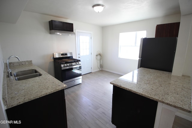 kitchen featuring stainless steel gas range oven, wood finished floors, freestanding refrigerator, light stone countertops, and a sink