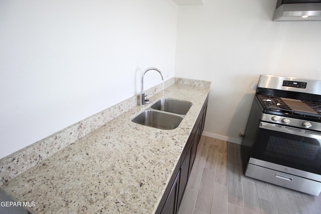 kitchen featuring light stone counters, stainless steel gas range, wood tiled floor, a sink, and exhaust hood