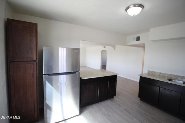 kitchen with light wood-style flooring, light stone counters, arched walkways, and freestanding refrigerator