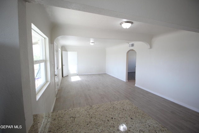 unfurnished room featuring arched walkways, visible vents, baseboards, and wood finished floors