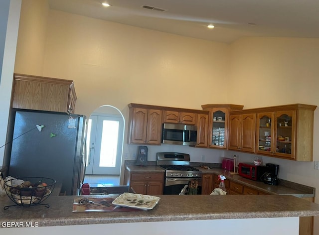 225 Peyton Rd, El Paso, TX 79928 - kitchen with stainless steel appliances, brown cabinets, arched walkways, glass insert cabinets, and a high ceiling