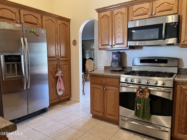 225 Peyton Rd, El Paso, TX 79928 - kitchen featuring appliances with stainless steel finishes, arched walkways, light tile patterned flooring, brown cabinetry, and dark countertops