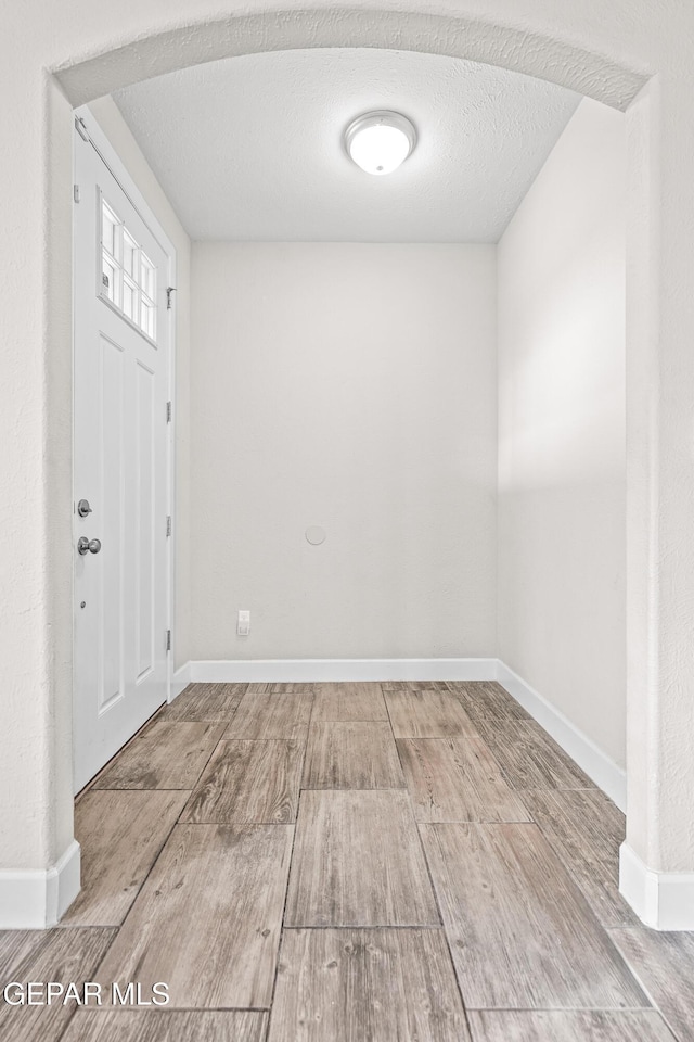 foyer entrance with a textured ceiling, arched walkways, wood finished floors, and baseboards