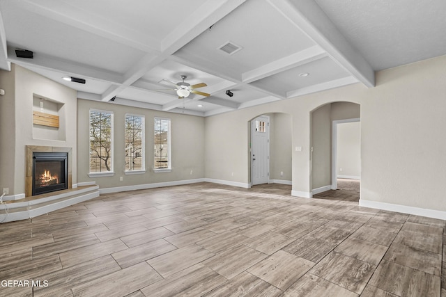 unfurnished living room featuring arched walkways, coffered ceiling, visible vents, baseboards, and a glass covered fireplace