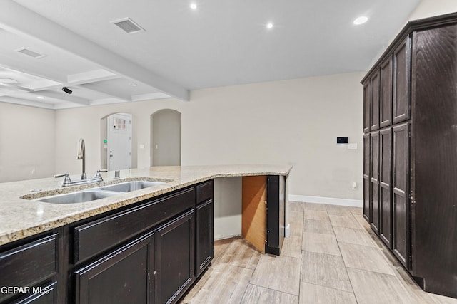 kitchen featuring arched walkways, light stone counters, a sink, visible vents, and beamed ceiling