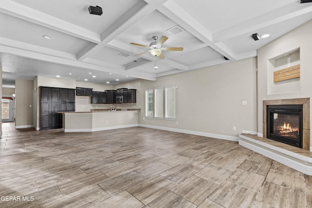 unfurnished living room with coffered ceiling, visible vents, baseboards, beamed ceiling, and a glass covered fireplace