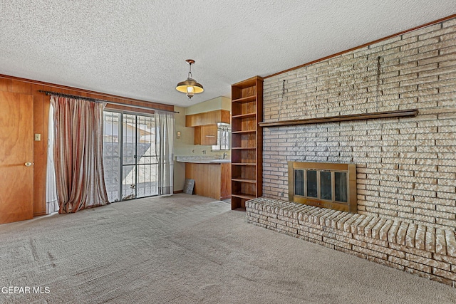 unfurnished living room featuring a sink, wood walls, a textured ceiling, a brick fireplace, and carpet flooring