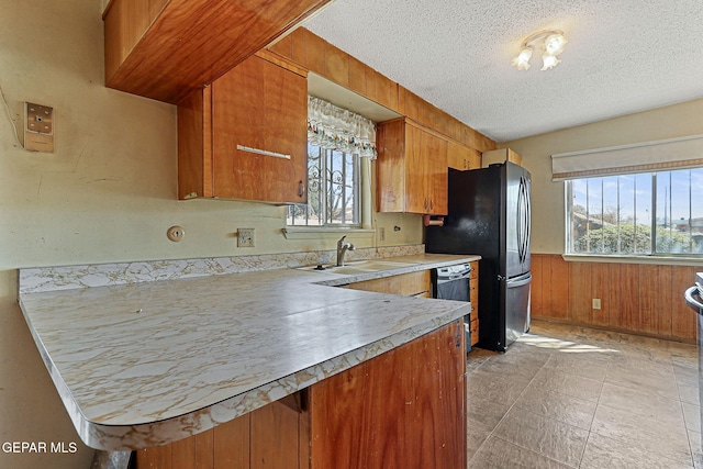 kitchen with wainscoting, a sink, light countertops, a textured ceiling, and brown cabinets