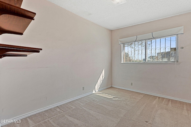 carpeted spare room featuring a textured ceiling and baseboards