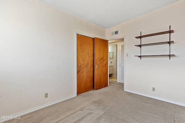 unfurnished bedroom featuring light carpet, visible vents, a textured ceiling, and baseboards