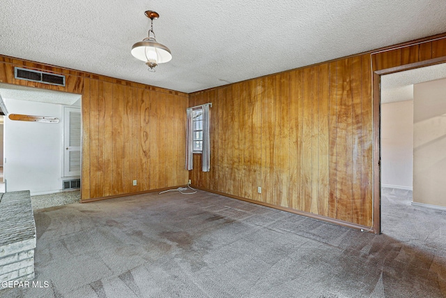 carpeted empty room with visible vents, wood walls, a textured ceiling, and baseboards