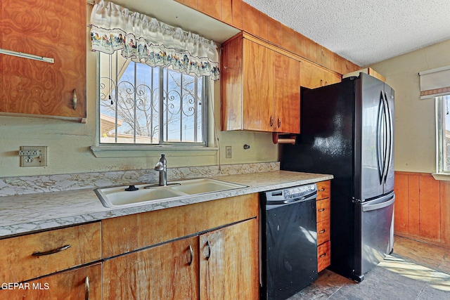 kitchen with a wainscoted wall, light countertops, black dishwasher, a textured ceiling, and a sink