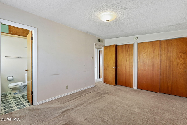 unfurnished bedroom featuring carpet, visible vents, ensuite bath, multiple closets, and a textured ceiling