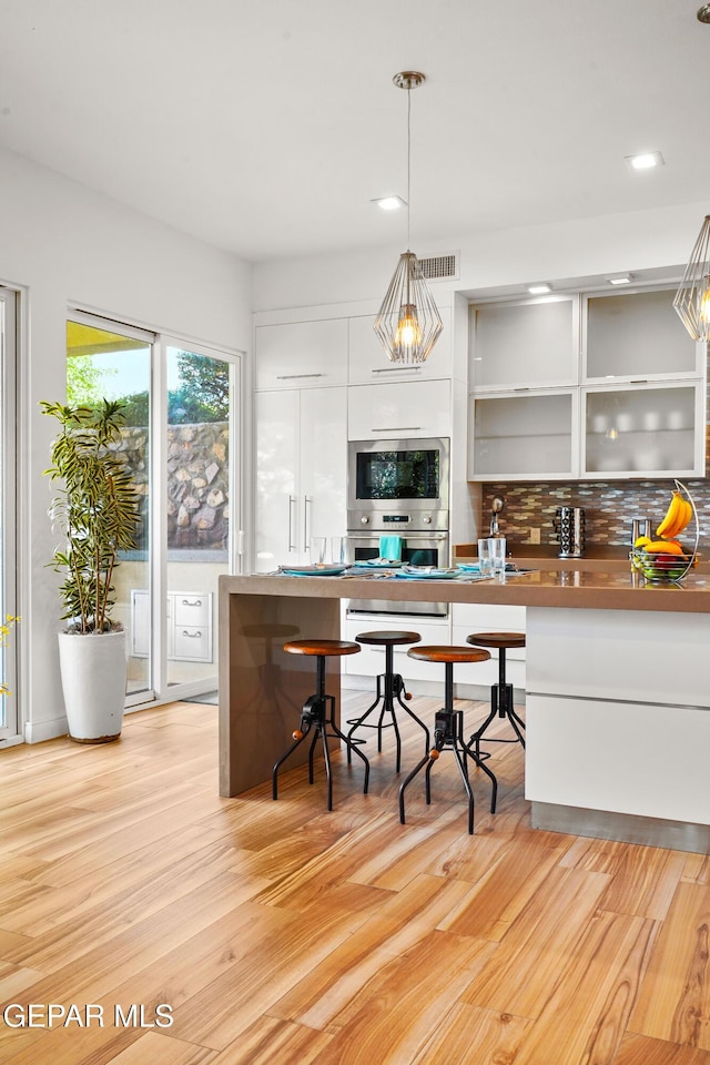 kitchen featuring visible vents, light wood-style floors, white cabinetry, decorative backsplash, and pendant lighting