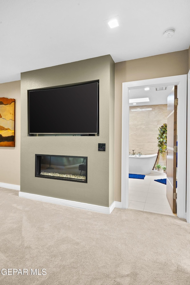 unfurnished living room with baseboards, carpet flooring, and a glass covered fireplace