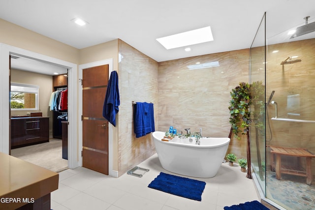 full bath with a skylight, tile walls, a soaking tub, a shower stall, and vanity